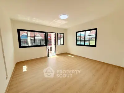 Spacious sunlit room with wooden flooring and large windows in modern home.