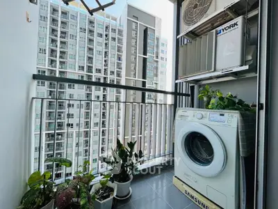 Modern apartment balcony with washing machine and plants, overlooking cityscape.