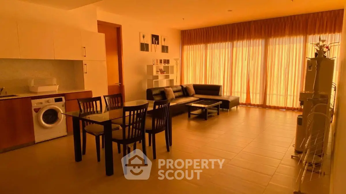 Spacious living room with modern furniture and natural light, featuring a dining area and washing machine.