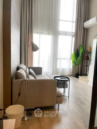 Modern living room with high ceilings and large windows, featuring a cozy sofa and stylish decor.