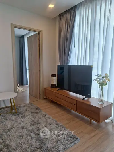 Modern living room with stylish decor and large TV, featuring cozy rug and elegant curtains.