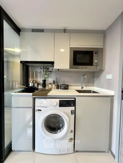 Modern compact kitchen with washing machine and microwave in sleek apartment
