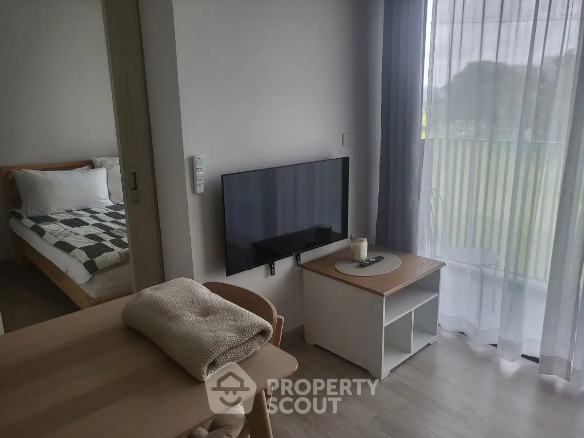 Cozy modern apartment with bedroom and living area, featuring a wall-mounted TV and balcony view.