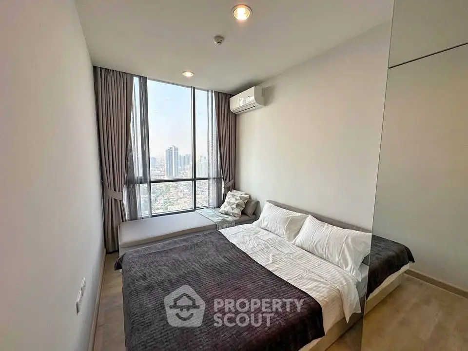 Modern bedroom with large window offering stunning city views in a high-rise apartment.