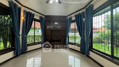 Spacious living room with large windows and elegant blue curtains, offering a serene garden view.