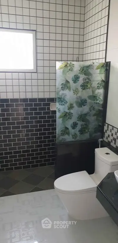 Modern bathroom with stylish black and white tiles and a tropical-themed shower curtain.