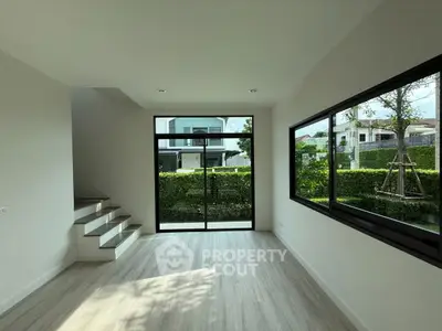 Modern living room with large windows and garden view, featuring sleek flooring and minimalist design.