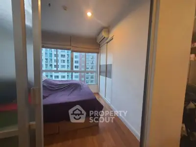 Modern bedroom with large window and city view, featuring wooden flooring and air conditioning.