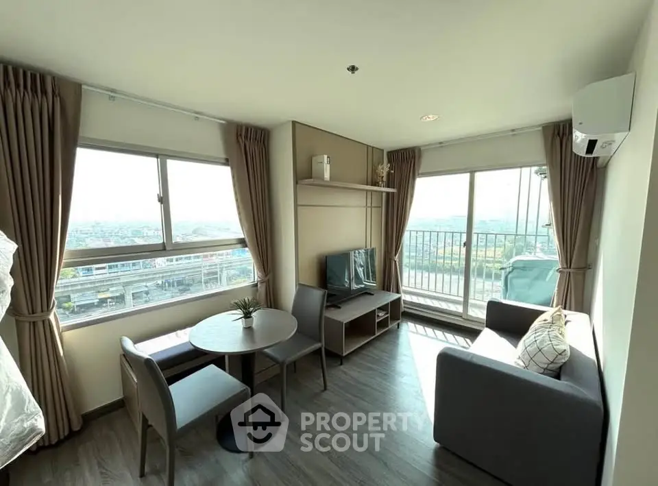 Modern living room with large windows and balcony offering stunning city views.