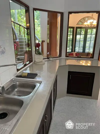 Spacious kitchen with dual sinks and large windows overlooking lush greenery