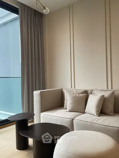 Modern living room with elegant beige sofa and stylish coffee tables near large window.