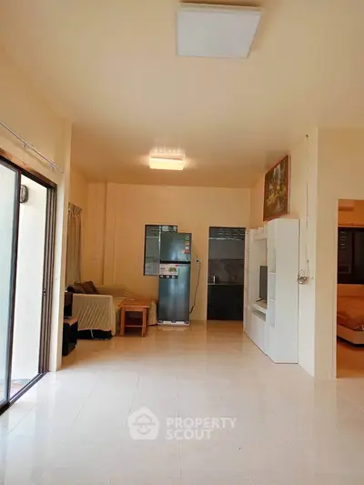 Spacious living room with modern decor and natural light, featuring a sleek refrigerator and stylish furniture.