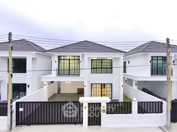 Modern white two-story house with gated entrance and large windows.