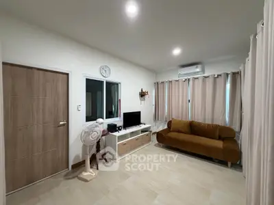 Cozy living room with modern decor, featuring a plush sofa, wall-mounted TV, and air conditioning.