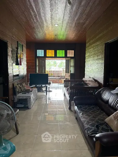Charming living room with wooden walls and colorful windows, featuring cozy seating and a TV area.