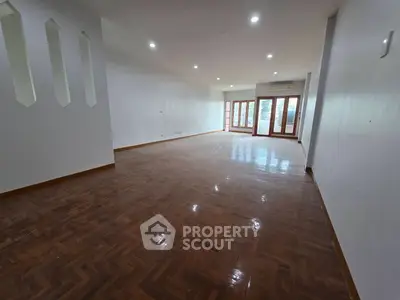 Spacious empty living room with polished wooden floors and large windows for natural light.