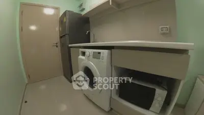 Compact kitchen with washing machine, fridge, and microwave in modern apartment.