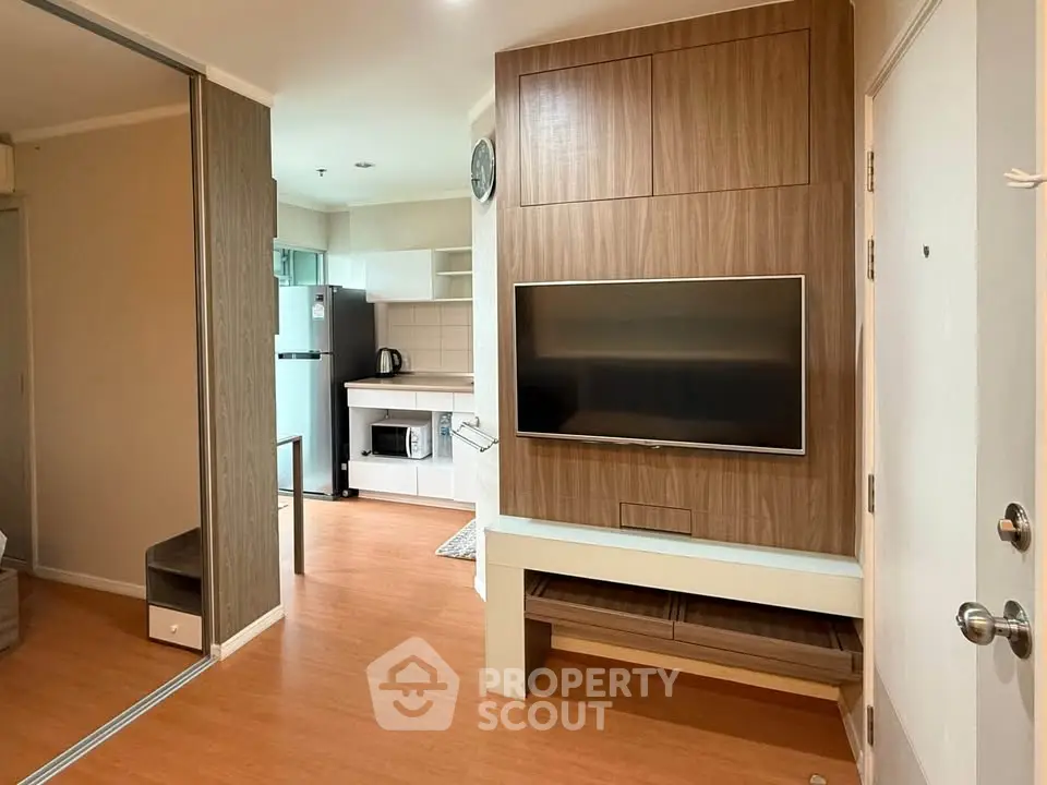 Modern apartment interior with open kitchen and stylish living area featuring wooden flooring and built-in TV unit.