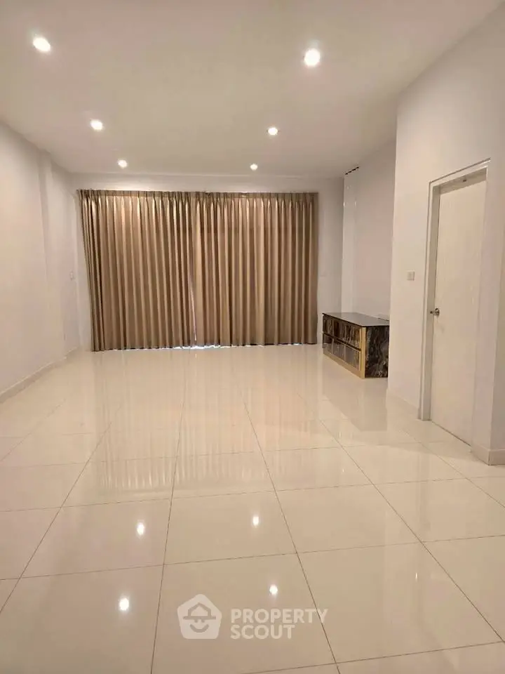 Spacious empty living room with glossy tiled floor and large window with curtains.