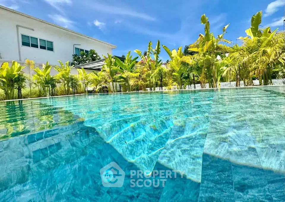Luxurious poolside view with lush greenery and modern architecture under a clear blue sky.