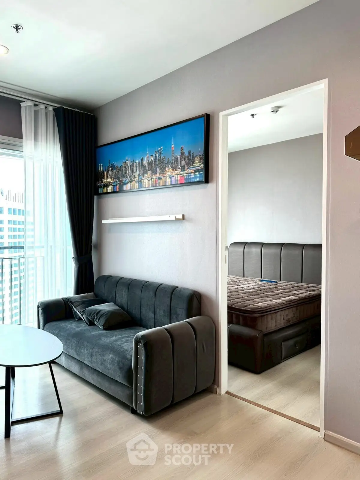 Modern living room with sleek sofa and cityscape artwork, adjacent to cozy bedroom in stylish apartment.
