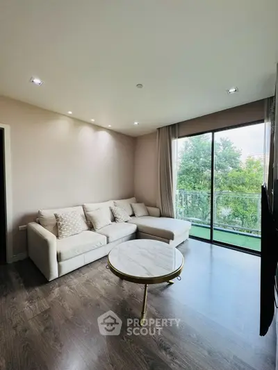 Modern living room with large windows and stylish furniture overlooking greenery.