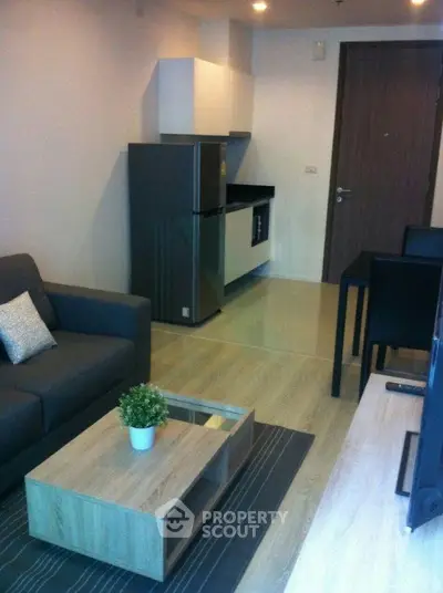 Modern living room with sleek furniture and compact kitchen in open layout apartment.