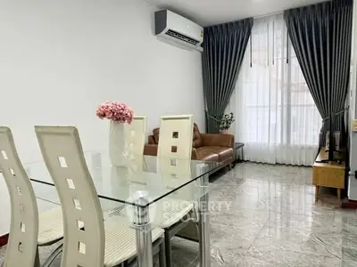 Modern living room with glass dining table, leather sofa, and elegant curtains.
