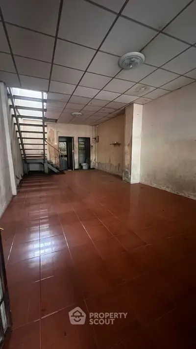 Spacious interior with tiled flooring and staircase, ideal for renovation or creative use.