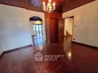 Spacious room with elegant wooden flooring and chandelier, featuring an arched doorway leading to a balcony.