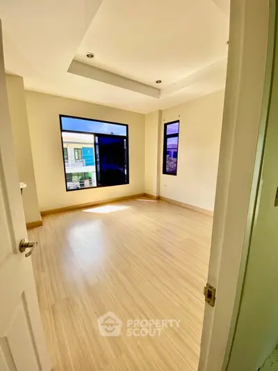 Spacious sunlit room with large windows and wooden flooring in modern home.