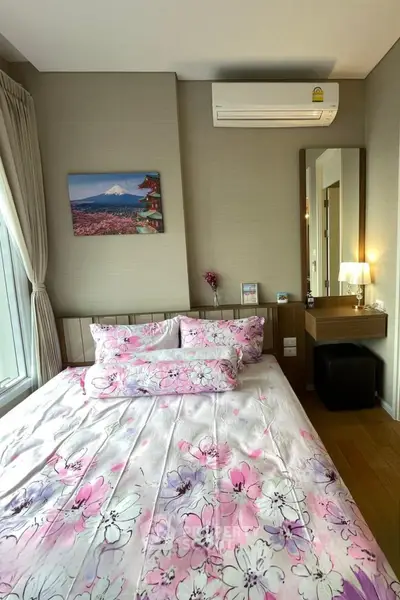 Cozy bedroom with floral bedding, air conditioning, and a scenic wall art, perfect for relaxation.