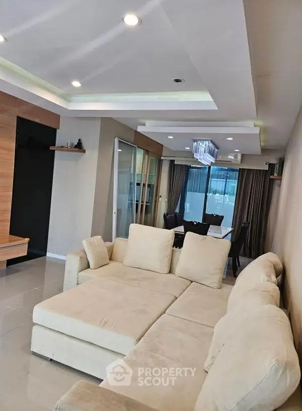 Spacious living room with modern beige sectional sofa and elegant dining area, perfect for entertaining.