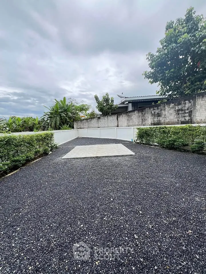 Spacious outdoor area with gravel surface and lush greenery, perfect for landscaping or outdoor activities.