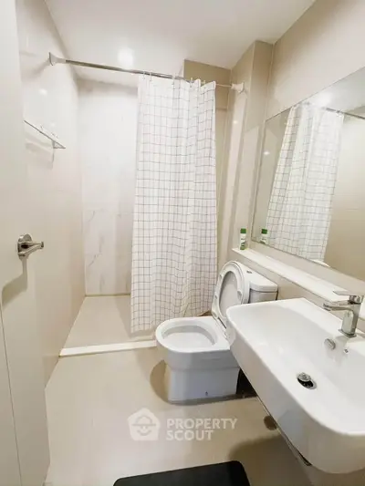 Modern bathroom with sleek fixtures and shower curtain in a contemporary apartment.