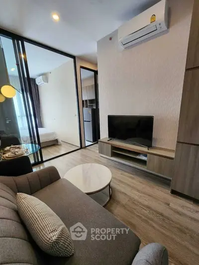 Modern living room with sleek furniture and glass partition leading to bedroom.