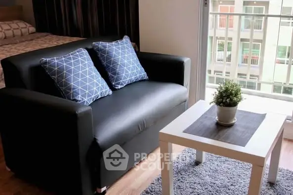 Cozy living area with black sofa, blue pillows, and a potted plant on a white table.
