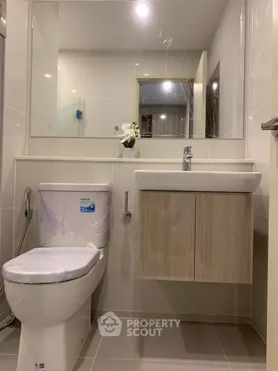 Modern bathroom with sleek fixtures and neutral tones, featuring a wall-mounted sink and large mirror.