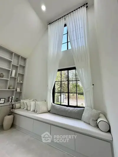 Elegant living room with high ceilings, large window, and cozy seating area with cushions.