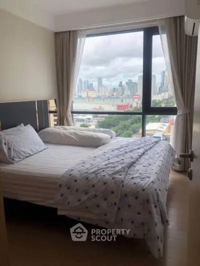 Cozy bedroom with city skyline view through large window, featuring modern decor and natural light.