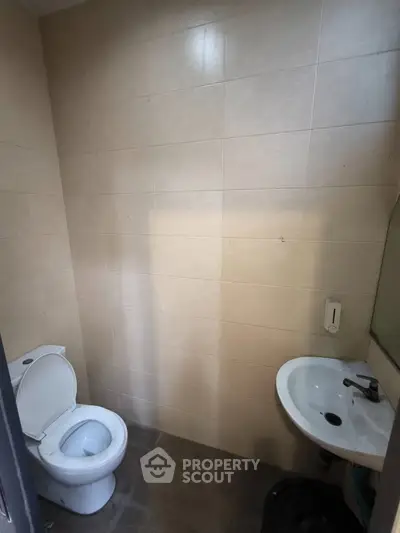 Compact bathroom with beige tiles, wall-mounted sink, and toilet in a cozy real estate property.