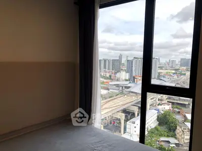 Cozy bedroom with stunning city view from large window, perfect urban living space.