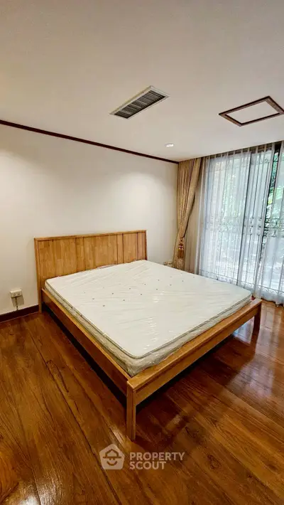 Spacious bedroom with wooden flooring and large window for natural light.