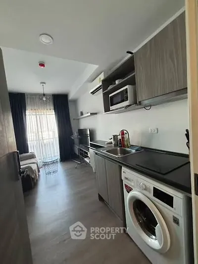 Modern studio apartment with sleek kitchen and washing machine, featuring a cozy living area and large window.