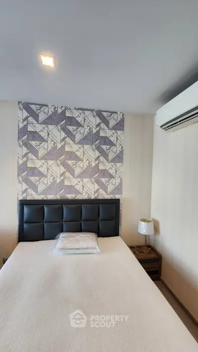 Modern bedroom with stylish wallpaper and air conditioning unit, featuring a comfortable bed and elegant bedside lamp.