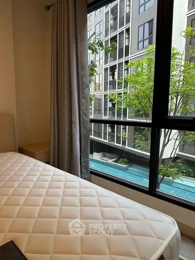 Cozy bedroom with a view of modern building and pool, perfect for urban living.