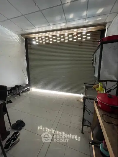 Spacious storage room with tiled floor and roller shutter door, ideal for versatile use.