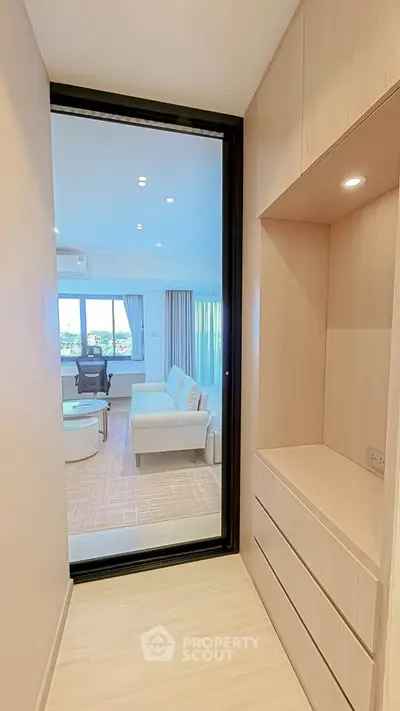 Modern apartment hallway leading to a bright living room with stylish furniture and large windows.