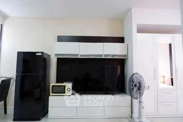 Modern living room with sleek furniture and appliances, featuring a black fridge and flat-screen TV.
