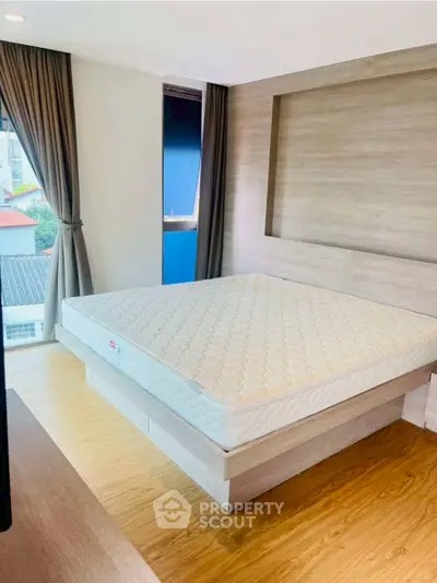 Modern bedroom with wooden flooring and large window offering natural light.